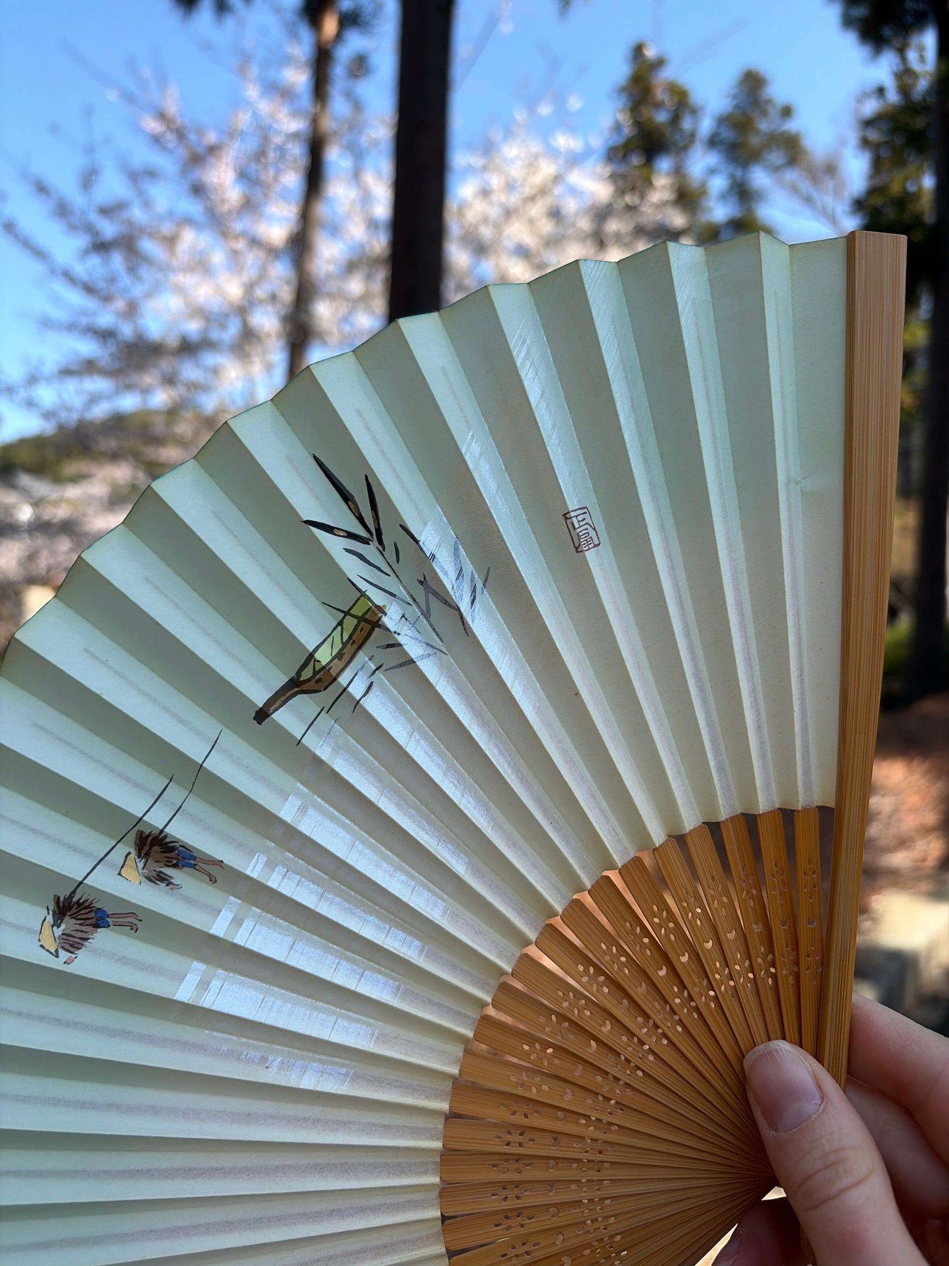 Open paper folding fan with a painted riverside scene
